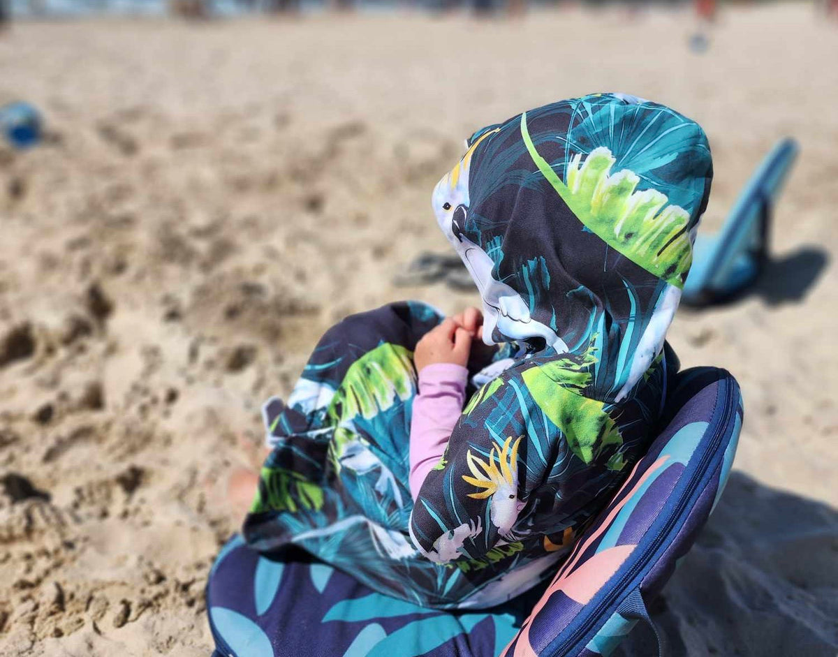 A boy sits and contemplates his next adventure with his Bird of Paradise sand less hood beach towel