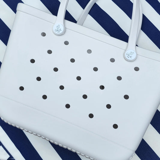 White Haven Silicone Bag: Beach Ready and Easy to Clean. [Durable white silicone bag rests on a blue and white striped beach towel, perfect for carrying your essentials and easy to clean up after a fun day at the beach.]