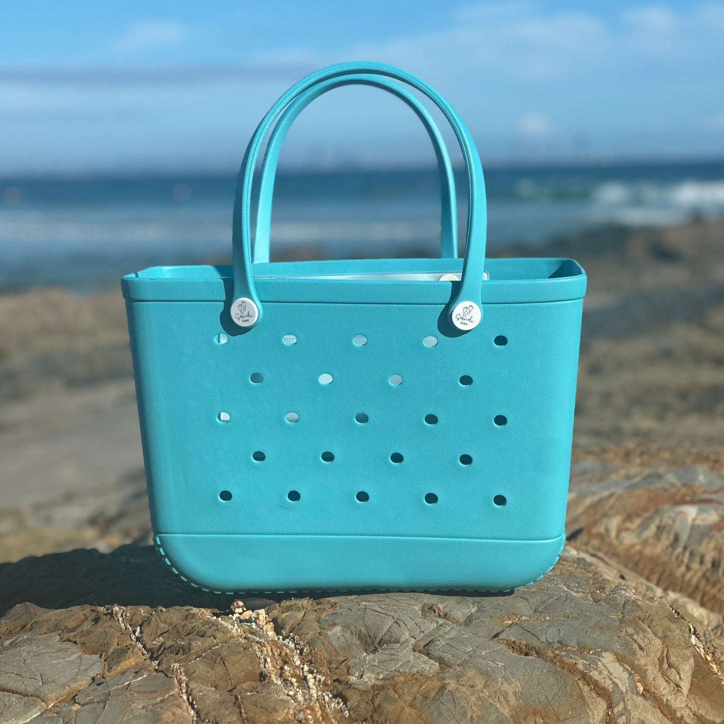 Aqua Marine Silicone Bag: Beach Essentials at Snapper Rocks. [Durable aqua marine silicone bag rests on the iconic rocks of Snapper Rocks, a world-famous surfing spot.]