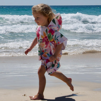 Girl (ages 3-6) wearing an Island Princess hooded beach hoodie (vibrant hibiscus flower design) with the hood flapping in the breeze as she runs happily along the beach at Currumbin, Queensland.