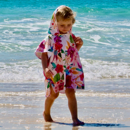 Girl (ages 3-6) wearing a Island Princess hooded beach towel featuring a vibrant design with hibiscus flowers. She is strolling along the beach with the hood up at Currumbin, Queensland.