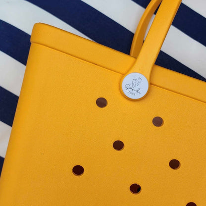 Yellow summer silicone bag showing sandi toes logo on a blue and white stripped towel