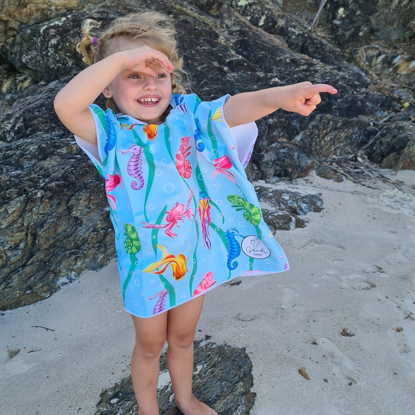 Currumbin Beach Queensland is the setting for this photo of a three year old girl wearing a sand free beach towel pointing out to sea