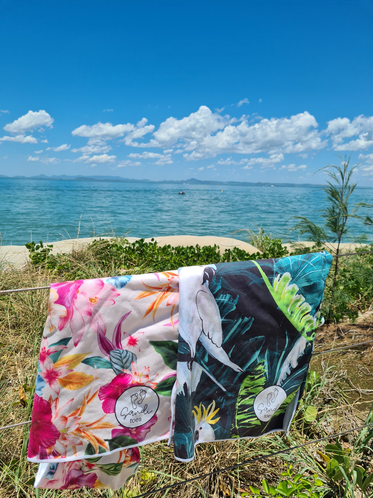 Sand free Beach Towels hanging on a fence at the beach, ocean and sand in the background, Island Princess and Bird of Paradise