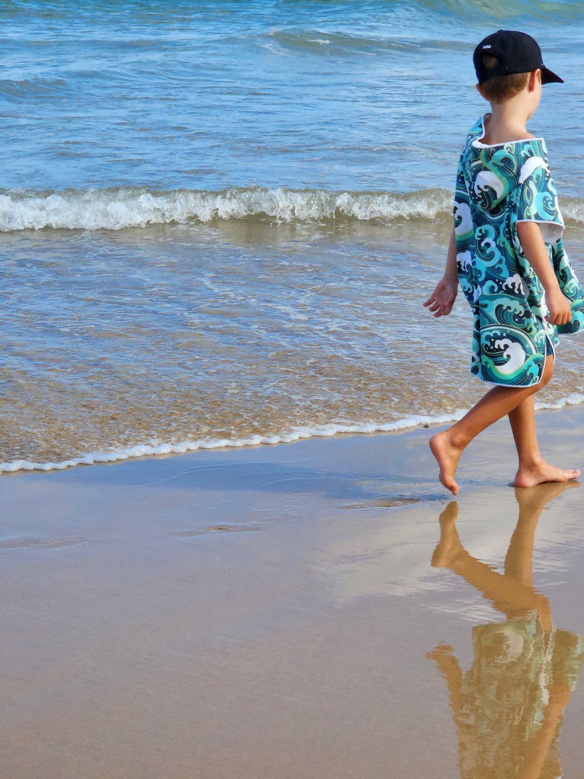 Yound boy walks along Currumbin Beach wearing his Wipeout designed towel he is approx 6 years old and wears the medium size