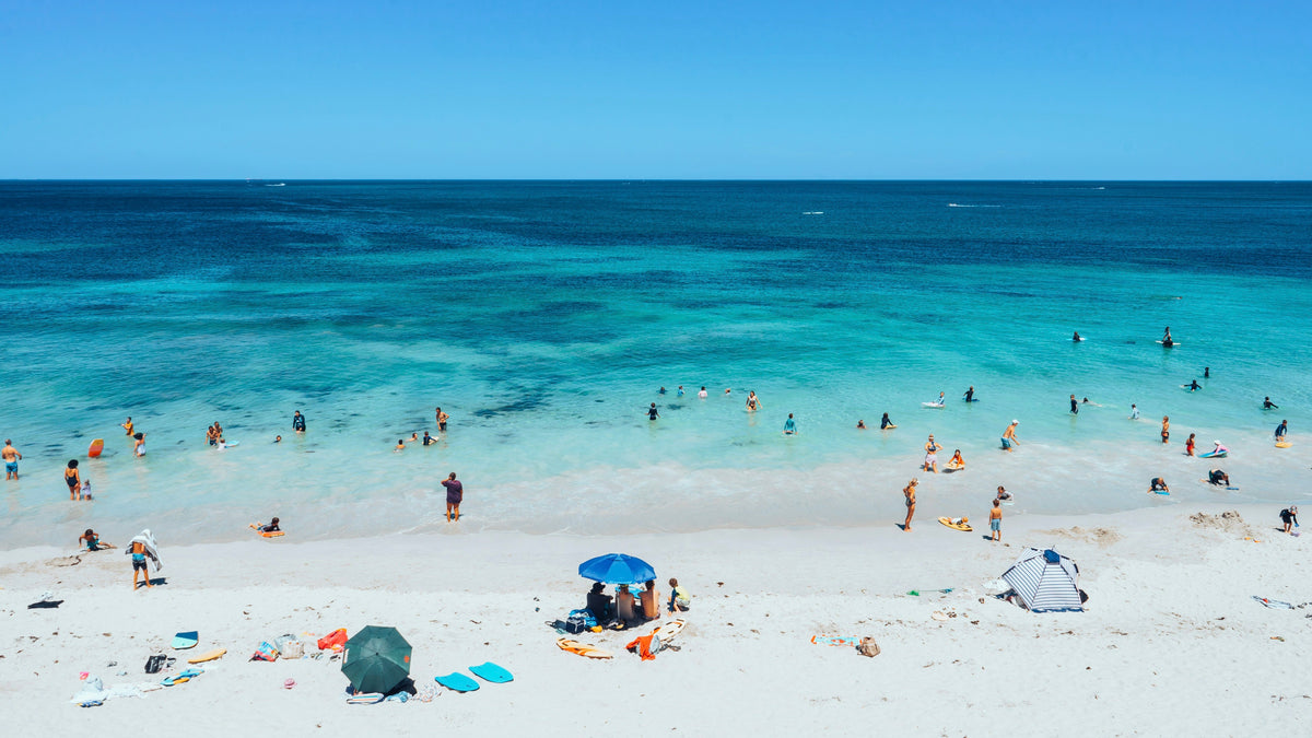 Group enjoying a day at Trigg Beach, Western Australia. Beachgoers relax on colorful Sandi Toes sand-free towels with a stylish silicone beach bag nearby.
