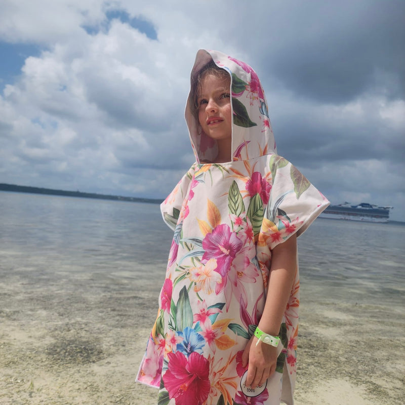 Child wearing a floral hooded towel on a beach with a cruise ship in the distance.