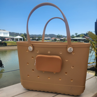 Sand EVA tote bag with a small pouch cup holder and clip with polka dot pattern on a wooden surface with a lake and buildings in the background