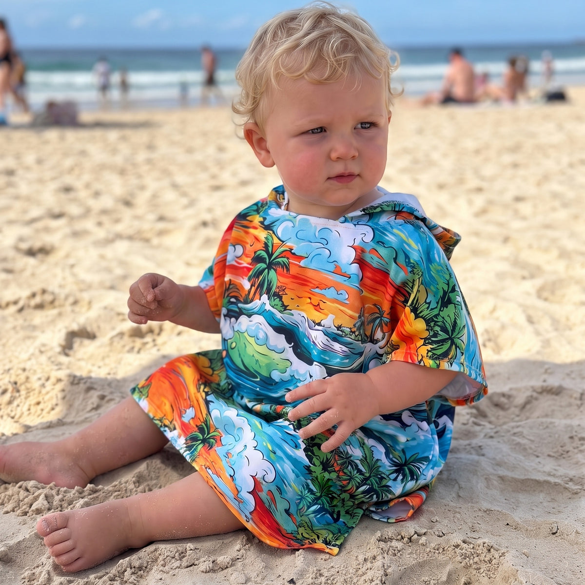 Baby wearing the Wave Rider sand-free hooded towel sitting on the beach